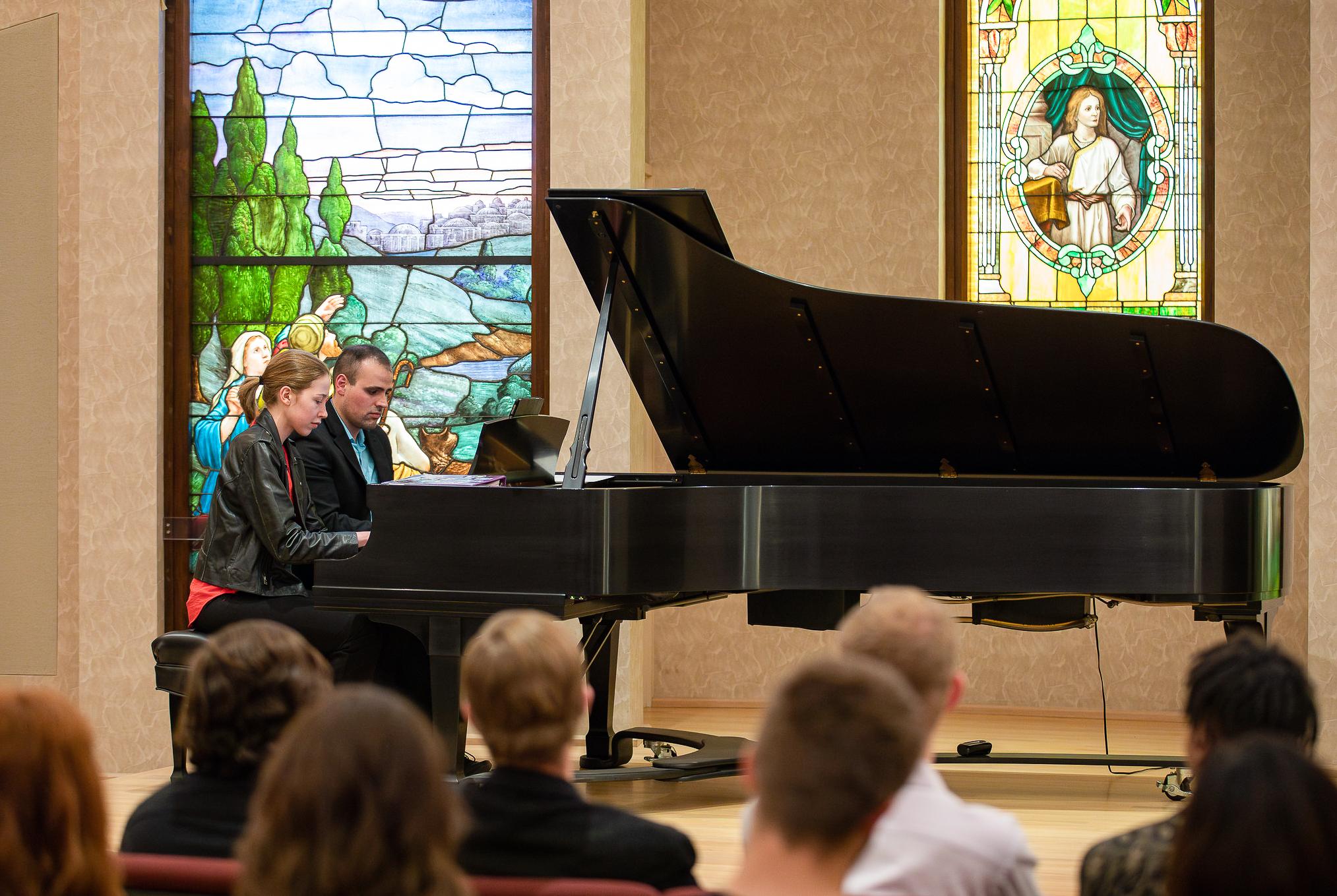 two people playing a grand piano side-by-side