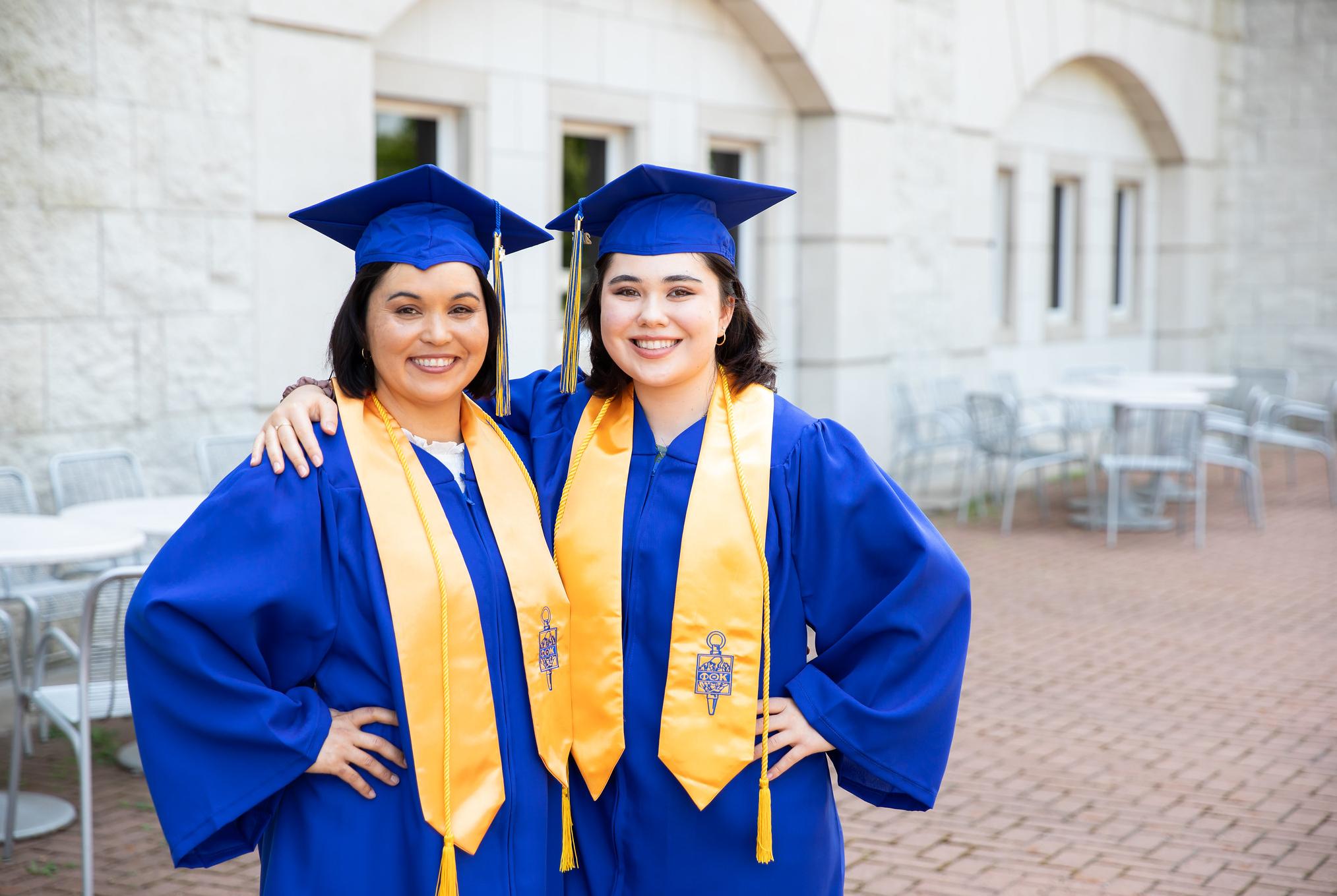 two graduates in caps and gowns mother and daughter posing for photo