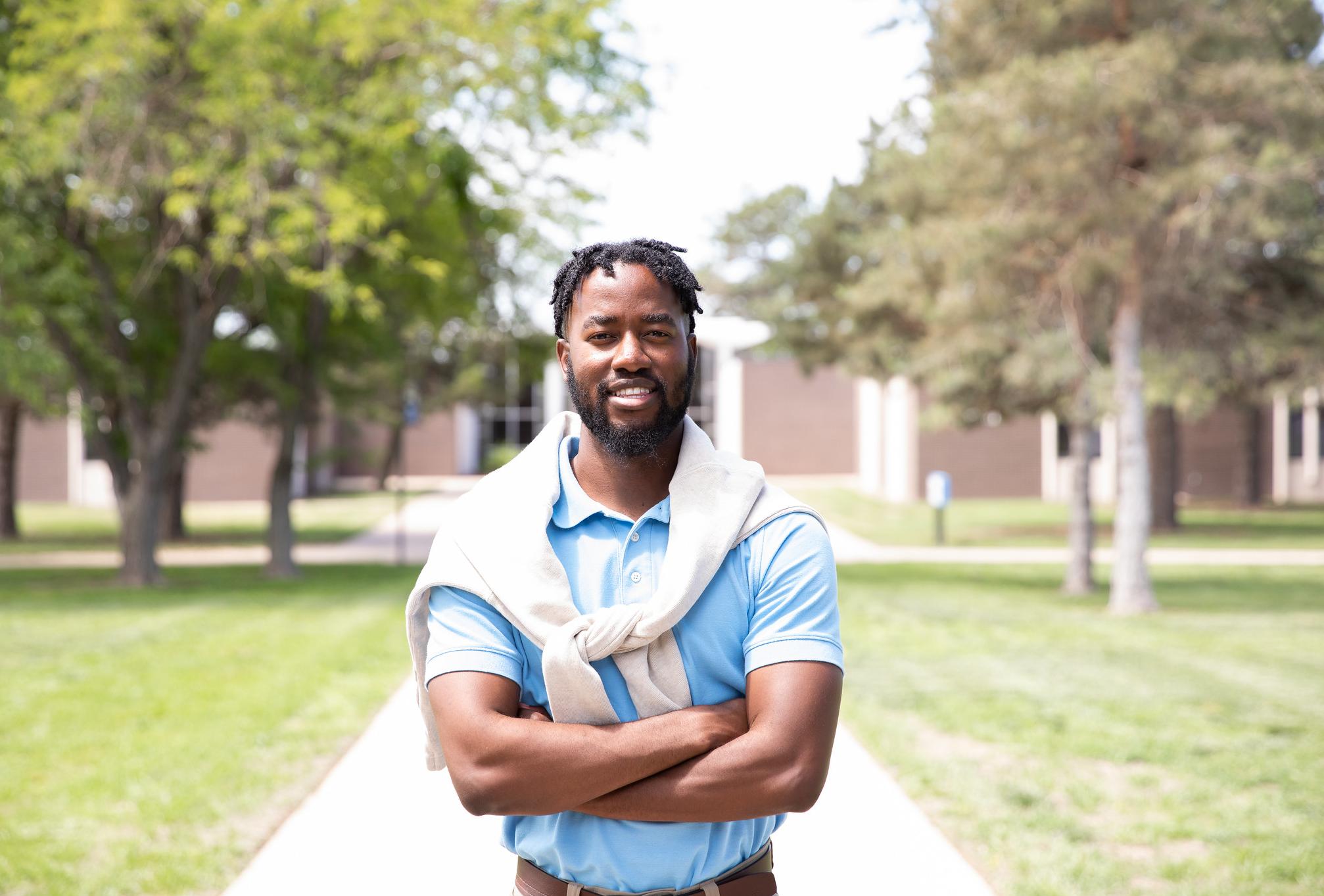 student standing in middle of sidewalk with campus building in background