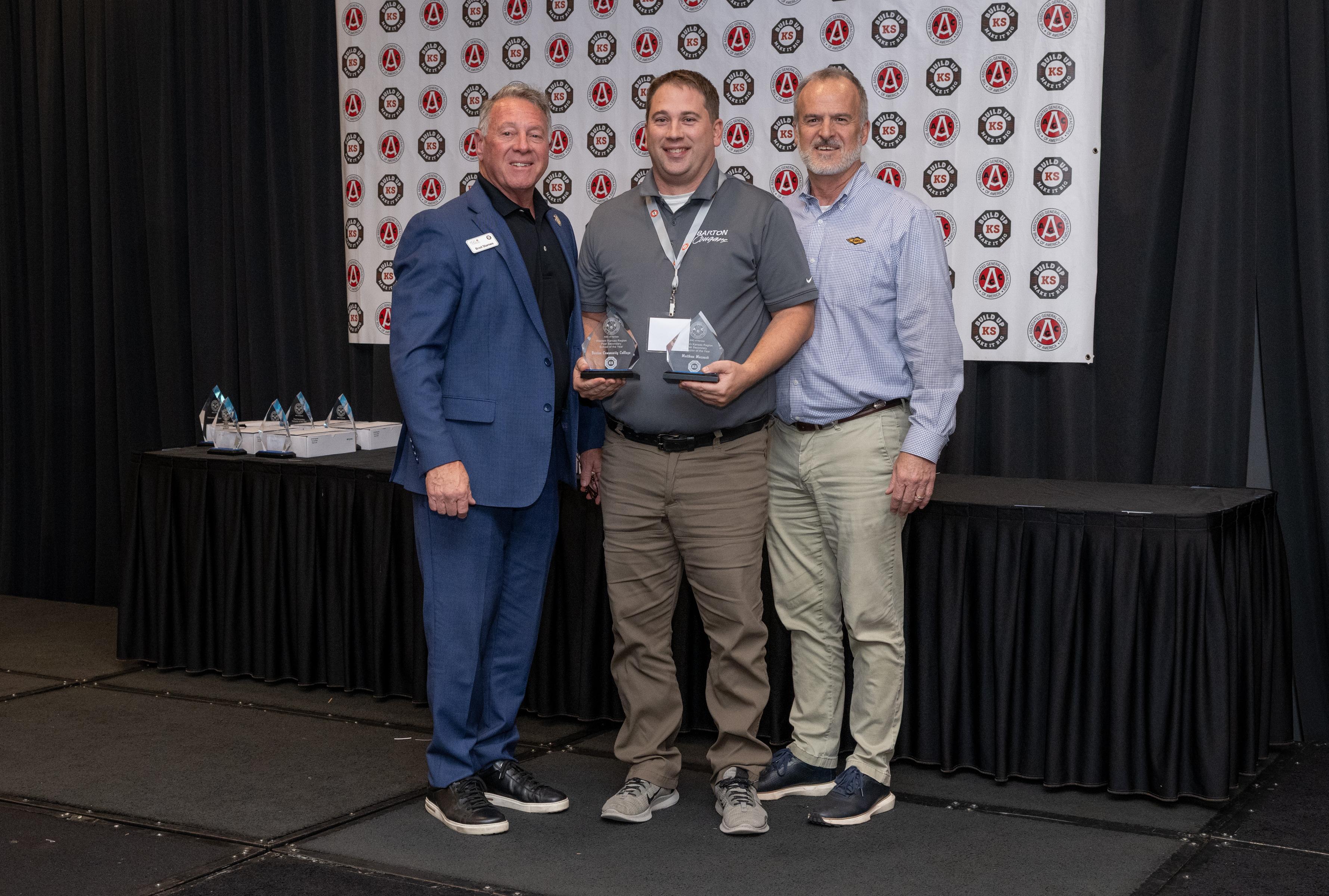three men standing on a stage with one holding two awards