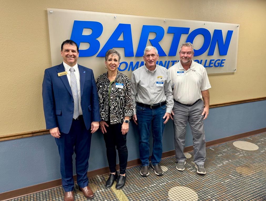four people standing in front of a college sign smiling