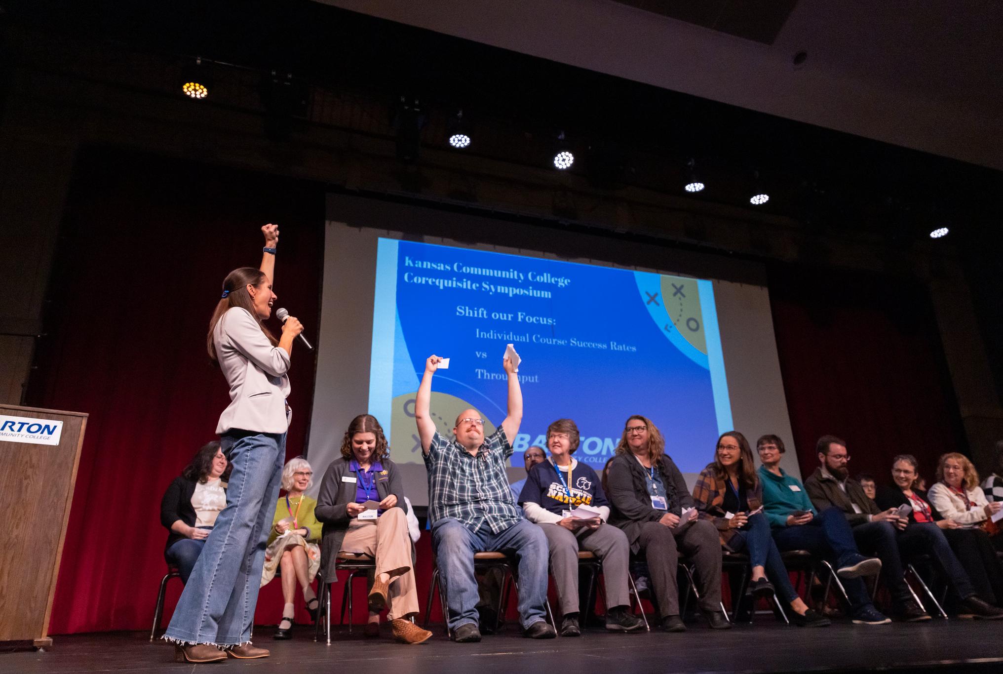 woman enthusiastically holding up her fist on stage while an audience member puts up both hands for winning a contest